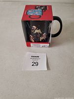 Photo of boxed black ceramic mug with Christmas dog illustrations and a lot number card in front of the mug box.