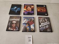 Six DVD cases arranged in two rows of three on a white surface: Stargate, MacGyver, Disturbed M.O.I. on top; Terminator, Superman, Fast & Furious on bottom.