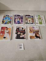 Photo shows seven Nintendo Wii game cases arranged in two rows. Titles visible include Disney's Magical Mirror, Karaoke Revolution, FIFA World Cup South Africa 2010, Wii Fit Plus, Wii Sports, The Bachelor Game, and Hannah Montana.