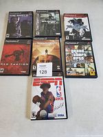 Top-down photo of seven PS2 game cases arranged in two rows showing game cover art clearly.