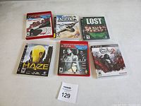Lot of six PlayStation 3 game cases displayed on a white surface. Titles visible include Need for Speed: Most Wanted, Blazing Angels 2: Secret Missions of WWII, Lost: Via Domus, Haze, Heavy Rain, and Silent Hill: Homecoming.