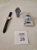 Photo showing three watches: one with black leather strap and white dial, one silver metal bracelet watch with dark dial, and one blue and white sport watch in original packaging.