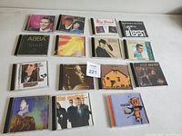Photo showing 15 various music CDs in jewel cases, arranged in three rows with visible cover art including ABBA, Steve Winwood, and others.