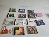 Photo of 14 various music CDs arranged in rows on a white surface, showing diverse album covers and artists.