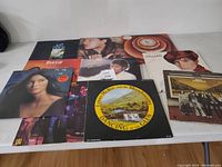 Photo of 10 various vinyl records laid out on a white table, showing front covers.