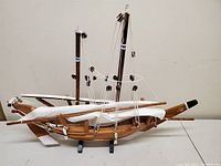 Front side view of wooden model ship with masts, rigging, sails folded on deck, and stand