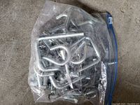 Clear plastic bag filled with numerous silver-colored metal hooks, including J-hooks, S-hooks, and bent bolts with threads.
