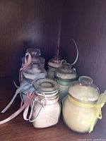Six glass jars filled with variously colored bath salts, with ribbons tied around the jars.