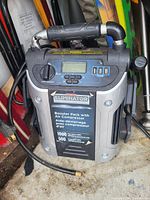 Photo showing the Eliminator booster pack with air compressor, control panel, digital display, jumper cables, and handle.