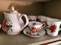 Teapot, four teacups with saucers, and four mugs all decorated with red poinsettias and gold trim.