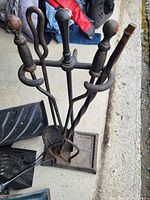 Overhead shot of a vintage iron fireplace tool set including poker, tongs, shovel, and brush on a square base stand with twisted handles.