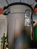 Gray Rubbermaid Roughneck garbage can with lid and labels on side, showing handles and top locking lid.