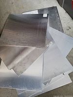 Seven flat metal sheets stacked in a staggered pile showing varied sizes and tones.