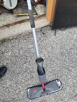 Full view of the Miele spray mop showing handle, spray trigger, and microfiber cleaning pad on paved surface.