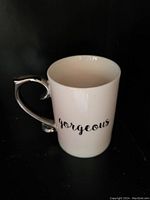 Photo of a white ceramic mug with a silver handle and 'gorgeous' text in black cursive font on side.