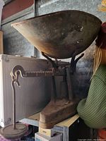 Old vintage baby scale showing metal weighing bowl, steel base, and horizontal balance arm with hook weight.