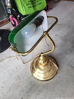Photo of a vintage brass desk lamp with a green shade and an exposed bulb inside. Lamp has a brass base and adjustable arm with pull chain switch.