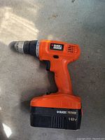 Orange Black & Decker cordless drill with 18V battery on concrete floor, showing side profile of drill.