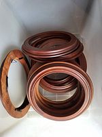 Multiple round wooden plate holders stacked in a container, showing their brown color and built-in foldable stands.