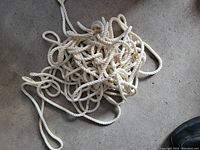 Single photo showing a loosely coiled bundle of white synthetic twisted rope on a concrete floor.