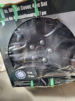 Four 17 inch diameter black plastic hubcaps in original packaging with slight damage to the box, front face showing curved spoke and lug nut design