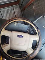 Image showing a beige and black Ford steering wheel with a worn brown leather grip cover and control buttons on the left spoke.