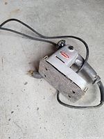 Photo showing an electric hand planer with grey metal body, black handle, power cord, and a worn base plate.