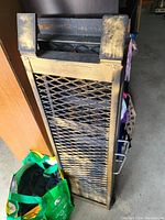 Single metal truck loading ramp with mesh surface leaning upright by a wooden cabinet.