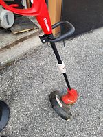 Red Homelite weedwacker string trimmer with loop handle and protective guard on trimmer head, on pavement surface.