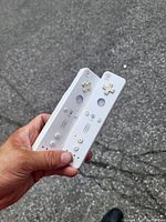 Two white Nintendo Wii Remote controllers held in hand, showing front face with buttons and speaker holes.