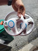Photo showing two white Wii steering wheels with blue accents held in hand outdoors.