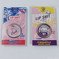Two tins of Lip Sh** lip balm in original packaging. One Strawberry Rhubarb flavor, one Pineapple Brown Sugar flavor.