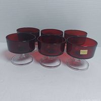 Front angled view showing six red stemmed glasses grouped together with one glass showing original label.