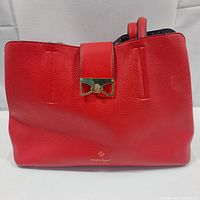 Front of red Nanette Lepore tote bag showing pebbled vegan leather texture and gold-tone bow clasp on center front strap