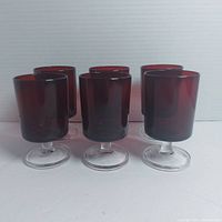 Front view showing six ruby red cylindrical goblets with clear pedestal bases arranged in two rows of three.