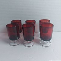 Front view of six amber red liqueur glasses showing upright glasses with clear stems and bases