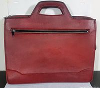 Front and back views of the vintage red vegan leather briefcase showing the integrated handle and zippered pocket.
