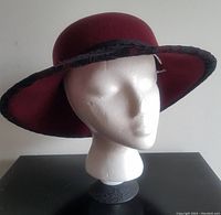 Side angle showing deep burgundy wool hat with wide brim covered in black lace, displayed on white mannequin head.