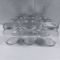 Front view of nine clear glass canning jars with silver metal screw lids arranged in a group on a white background.