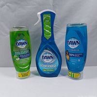 Three bottles of Dawn dishwashing products: two bottles of Dawn Ultra EZ-Squeeze Dishwashing Liquid (green and blue, 443 ml each) and one bottle of Dawn Ultra Platinum Powerwash Dish Spray (473 ml, apple scent).
