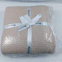 Packaged beige woven waffle blanket with branded white ribbon.