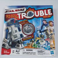 Photo of sealed game box with Star Wars Pop-O-Matic Trouble featuring R2-D2 and character artwork, indicating electronic sounds and age 5+.