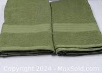 Two folded green 100% cotton bath towels side by side showing texture and band detail