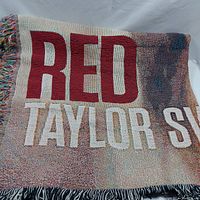 Close-up of woven text 'RED TAYLOR SWIFT' on blanket with fringe finish.