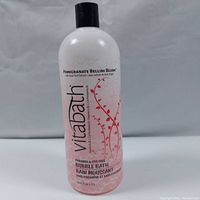 Front view of a clear plastic bottle with pink bubble bath liquid inside, black cap, and floral design label.