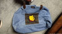 Blue denim bag with plaid front pocket featuring Winnie the Pooh face appliqué.