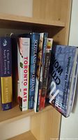 Photo showing the spines of six books on a shelf: A Short History of Nearly Everything by Bill Bryson, Toronto Eats, Scotland and Her Tartans, Kitchen Cabinet Cures, Nomad, 100 Most Beautiful Cities in the World