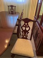 Four cherrywood dining chairs with upholstered cream-colored seats around a matching cherrywood dining table. One chair is a captain's chair with arms.
