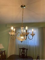 Full view of chandelier hanging from ceiling illuminating 5 bulbs in candle style, brass finish metal with ribbed glass detail.