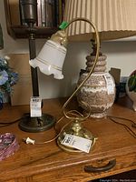 Brass desk lamp with curved metal base and white glass shade with gold accent lines. Cord and plug visible on wood surface.